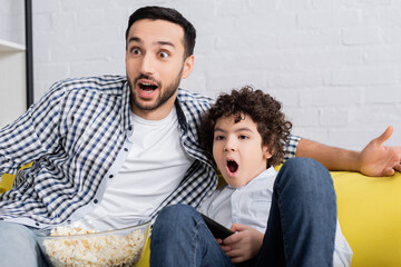 Wall Mural - astonished muslim father and son watching tv near popcorn at home