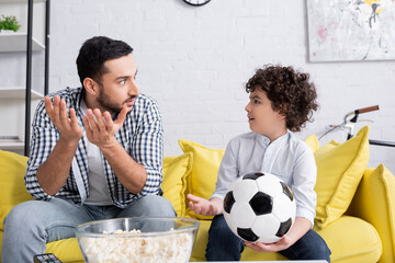 Wall Mural - surprised muslim father and son looking at each other while watching football match at home