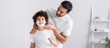 Arabian Man Applying Shaving Foam On Face Of Son With Razor, Banner