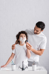 Wall Mural - Father teaching arabian son in shaving foam with razor in bathroom