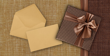 Gift card with gift box with ribbon and bow, envelope and ticket, isolated on elegant brown fabrics background, top view and copy space template, layout useful for best wishes and shopping concept