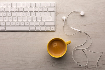 Smart working concept. Top view of a white wooden table with  a cup of coffee, computer keyboard and earphones on it.