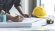 © Puwasit Inyavileart - Architectural building design and construction plans with blueprints, Young man was designing a building or architecture with a ruler, pen, pencil, tape measure, architect hat.