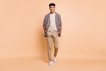 Full size photo of brunet optimistic guy going wear modern shirt trousers sneakers isolated on beige color background