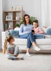 people, family and technology concept - happy mother and two daughters with smartphone at home