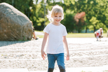 Wall Mural - Cute cheerful girl playing in fountain. Kid in white shirt having fun in summer park