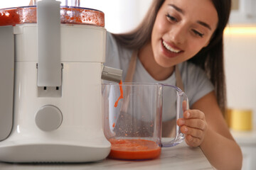 Wall Mural - Young woman making tasty fresh juice at table in kitchen, closeup