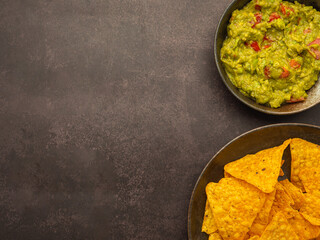 Wall Mural - Fresh guacamole and tortilla chips on a plate placed on dark brown background with copy space for text. Top view. Concept of traditional Mexican foods and healthy fruits