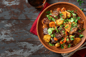 Goulash. Beef stew with potatoes, onions, carrots and spices in a ceramic plate on a dark wooden table top view. Rustic style. Stewed meat with vegetables. Copy space for text