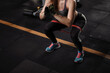 Cropped shot of a sportswoman doing glutes workout, squatting with resistance band at the gym