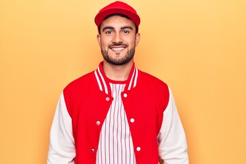 Wall Mural - Handsome sporty man with beard wearing baseball jacket and cap over yellow background with a happy and cool smile on face. Lucky person.
