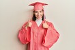 © Krakenimages.com - Young caucasian woman wearing graduation cap and ceremony robe success sign doing positive gesture with hand, thumbs up smiling and happy. cheerful expression and winner gesture.