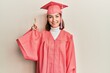 © Krakenimages.com - Young caucasian woman wearing graduation cap and ceremony robe showing and pointing up with finger number one while smiling confident and happy.