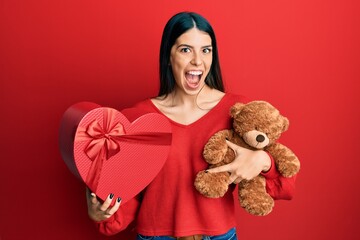 Wall Mural - Young hispanic woman holding valentine gift celebrating crazy and amazed for success with open eyes screaming excited.