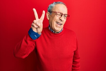 Wall Mural - Handsome senior man with grey hair wearing casual clothes and glasses smiling with happy face winking at the camera doing victory sign. number two.