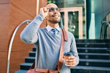 Wall Mural - Young african american businessman smiling happy and drinking take away coffee at the city.