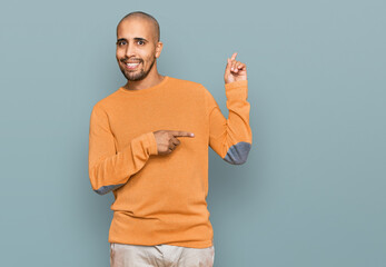 Poster - Hispanic adult man wearing casual winter sweater smiling and looking at the camera pointing with two hands and fingers to the side.