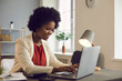 © Studio Romantic - Young afro american businesswoman working on laptop with electronic documents sitting in the office. Smiling woman typing on the keyboard by sending an email or filling out an electronic database.