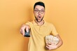 © Krakenimages.com - Young hispanic man eating popcorn using tv control afraid and shocked with surprise and amazed expression, fear and excited face.