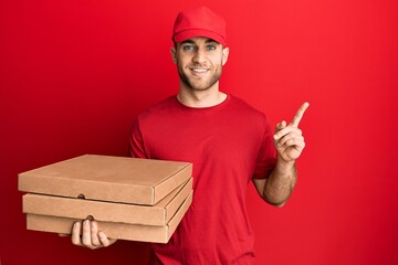 Poster - Young caucasian man holding delivery pizza box smiling happy pointing with hand and finger to the side