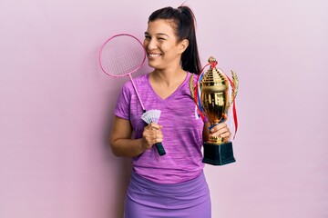 Poster - Young latin woman holding badminton racket and trophy winking looking at the camera with sexy expression, cheerful and happy face.