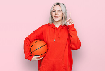 Poster - Young blonde girl holding basketball ball surprised with an idea or question pointing finger with happy face, number one