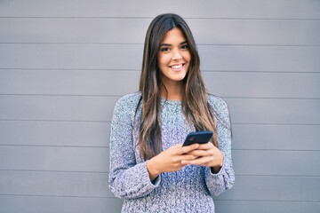 Poster - Young beautiful hispanic girl smiling happy using smartphone at the city.