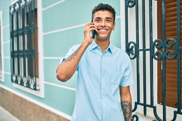 Poster - Young latin man smiling happy using smartphone walking at the city.