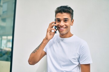 Poster - Young latin man smiling happy talking on the smartphone walking at the city.