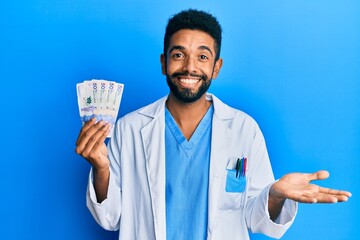 Poster - Handsome hispanic man with beard wearing doctor uniform holding 50 colombian pesos celebrating achievement with happy smile and winner expression with raised hand