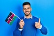 © Krakenimages.com - Young hispanic man with beard holding kenya flag smiling happy and positive, thumb up doing excellent and approval sign
