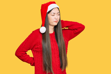 Wall Mural - Young chinese woman wearing christmas hat suffering of neck ache injury, touching neck with hand, muscular pain