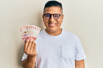 Canvas Print - Young latin man holding 10 colombian pesos banknotes looking positive and happy standing and smiling with a confident smile showing teeth