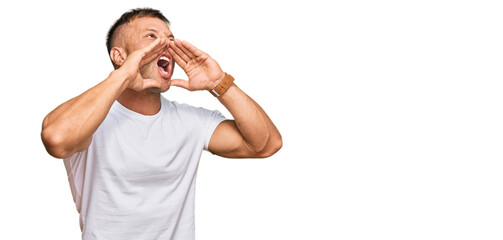 Canvas Print - Handsome muscle man wearing casual white tshirt shouting angry out loud with hands over mouth