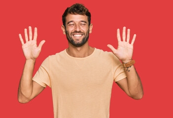 Poster - Handsome young man with beard wearing casual tshirt showing and pointing up with fingers number ten while smiling confident and happy.