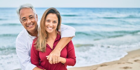 Canvas Print - Middle age hispanic couple smiling happy and hugging walking at the beach