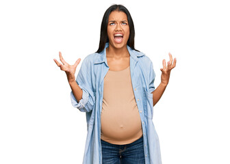 Sticker - Beautiful hispanic woman expecting a baby showing pregnant belly crazy and mad shouting and yelling with aggressive expression and arms raised. frustration concept.