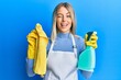 © Krakenimages.com - Beautiful blonde woman wearing cleaner apron holding cleaning products winking looking at the camera with sexy expression, cheerful and happy face.