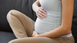 © LIGHTFIELD STUDIOS - cropped view of pregnant woman touching belly on couch at home