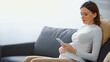 young pregnant woman sitting on couch and messaging on smartphone