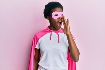 Sticker - Young african american girl wearing superhero mask and cape costume shouting and screaming loud to side with hand on mouth. communication concept.