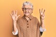 © Krakenimages.com - Senior grey-haired woman wearing casual clothes and glasses showing and pointing up with fingers number eight while smiling confident and happy.