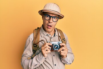 Wall Mural - Middle age bald man wearing explorer hat and vintage camera in shock face, looking skeptical and sarcastic, surprised with open mouth