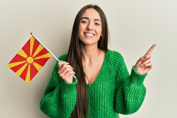 Sticker - Young hispanic girl holding macedonian flag smiling happy pointing with hand and finger to the side