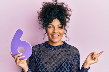 Poster - Young hispanic woman holding number six smiling happy pointing with hand and finger to the side