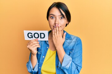 Beautiful young woman with short hair holding paper with god word covering mouth with hand, shocked and afraid for mistake. surprised expression