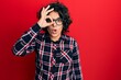Young hispanic woman with curly hair wearing casual clothes and glasses doing ok gesture shocked with surprised face, eye looking through fingers. unbelieving expression.