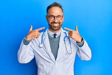 Sticker - Handsome middle age man wearing doctor uniform and stethoscope smiling cheerful showing and pointing with fingers teeth and mouth. dental health concept.