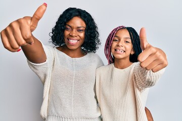 Poster - Beautiful african american mother and daughter wearing casual clothes and hugging approving doing positive gesture with hand, thumbs up smiling and happy for success. winner gesture.