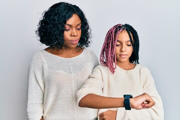 Canvas Print - Beautiful african american mother and daughter wearing casual clothes and hugging checking the time on wrist watch, relaxed and confident